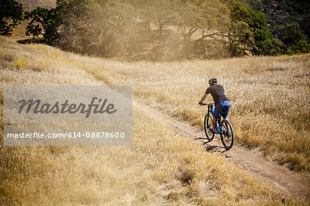 Elevated rear view of young man mountain biking on dirt track, Mount Diablo, Bay Area, California, USA