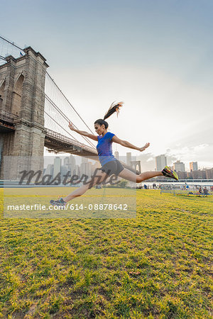 Young woman training in front of Brooklyn bridge, New York, USA