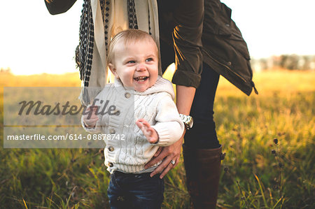 Mid section of mother bending over supporting standing smiling baby boy