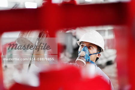 Close up of male factory worker spray painting a red crane in factory workshop, China