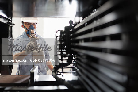 Male worker spray painting components black in crane factory spray booth, China