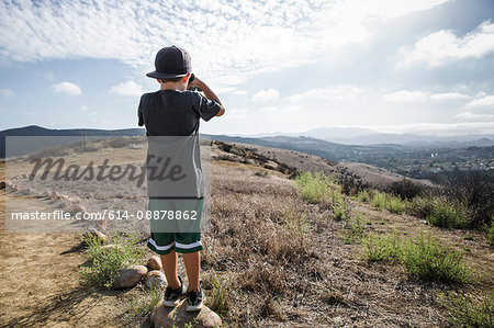 Rear view of boy looking through binoculars from footpath stone, Thousand Oaks, California USA