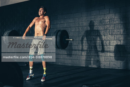 Male crossfitter weight training lifting barbell in gym