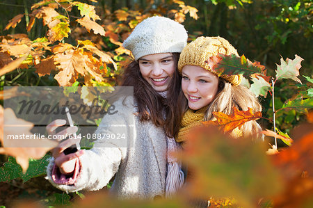 High angle view of teenage girls among autumn leaves using smartphone to take selfie smiling