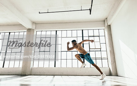 Side view of young man in gym doing powerful running stance