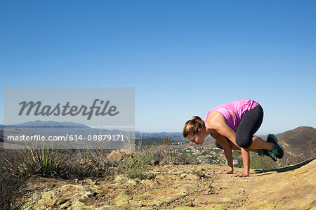 Mature woman practicing yoga pose on top of hill