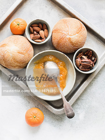 Overhead view of bread rolls with marmalade and bowls of nuts