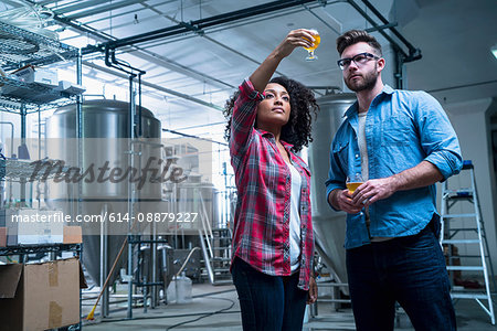 Colleagues in brewery holding up glass of beer, checking quality