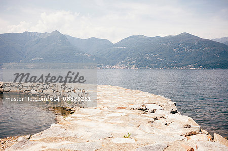 Stone pier curving through water by mountain range, Luino, Lombardy, Italy