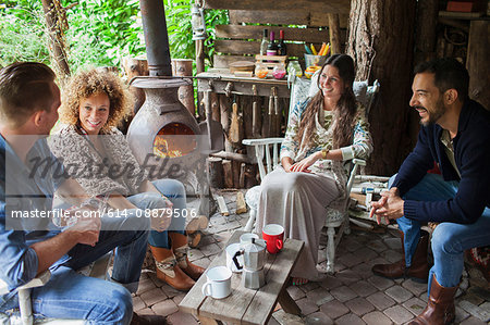 Four adult friends drinking coffee in open cabin with wood stove