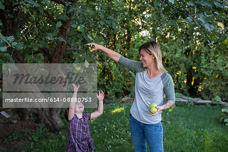 Mother helping daughter reach apple on tree