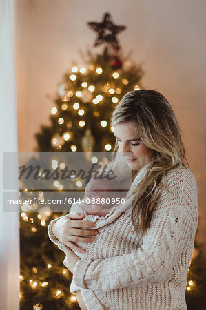 Mid adult woman cradling new born baby daughter wrapped in cardigan at Christmas