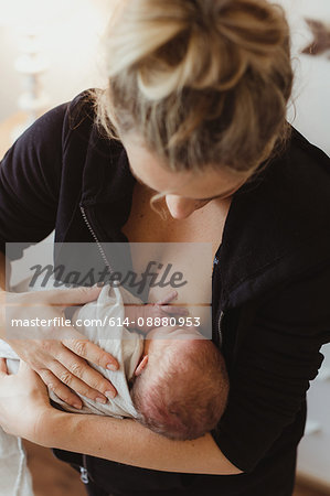 Mid adult woman breast feeding newborn baby daughter