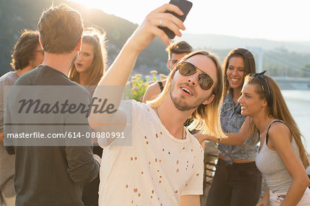 Young man taking selfie at waterfront roof terrace party, Budapest, Hungary