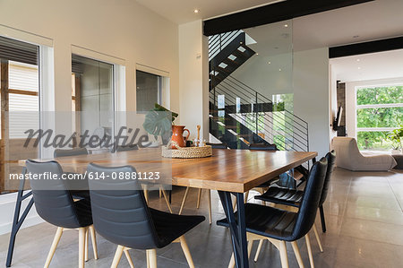American walnut wood dining table and black leather sitting chairs with ash wood legs in the dining room inside a modern cube style home, Quebec, Canada
