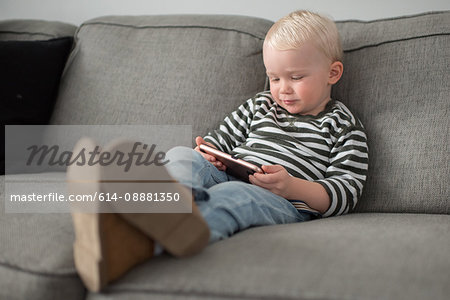 Young boy sitting on sofa, looking at smartphone