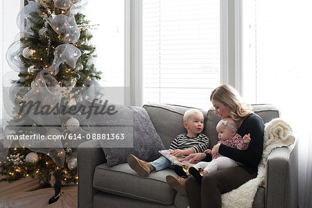 Mother and children sitting on sofa, looking at book