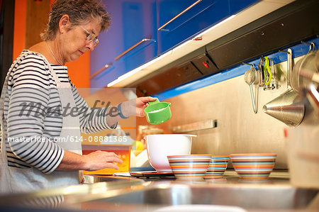 Senior woman in kitchen, measuring ingredients into mixing bowl