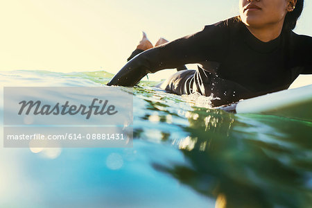 Young female surfer paddling surfboard at sea, Newport Beach, California, USA