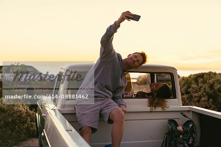 Man taking smartphone selfie with girlfriend in back of pickup truck at Newport Beach, California, USA