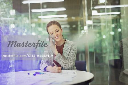 Smiling businesswoman talking on cell phone and taking notes in conference room