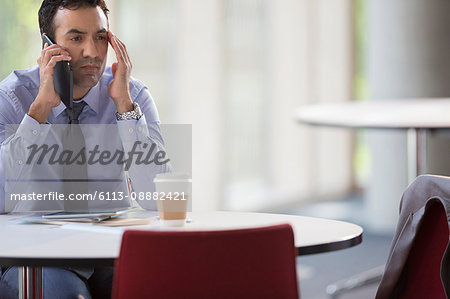 Stressed businessman talking on cell phone at table