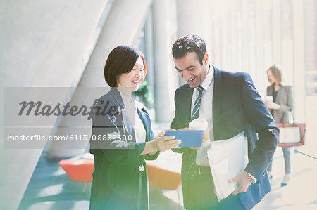 Businessman and businesswoman reviewing paperwork in sunny office lobby