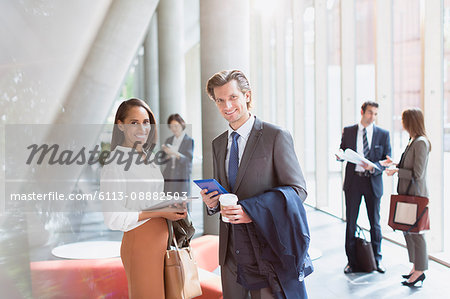 Portrait smiling businessman and businesswoman in sunny office lobby