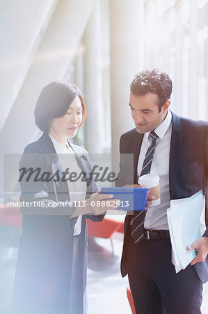 Business people using digital tablet in sunny office lobby