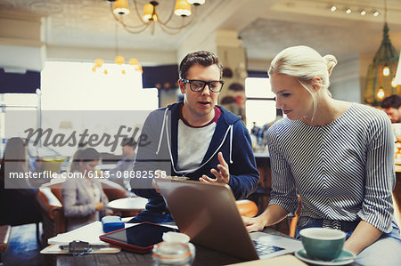 Creative business people using laptop in cafe