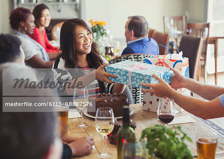 Smiling woman receiving birthday gift from friend at restaurant table