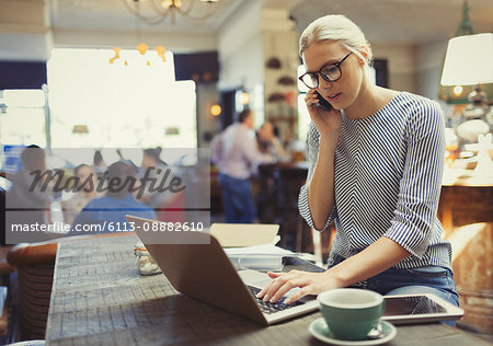 Creative businesswoman talking on cell phone and using laptop in cafe