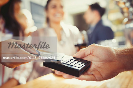 Woman with credit card paying bartender with contactless payment at bar