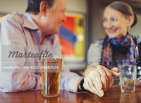 Senior couple holding hands drinking beer at bar