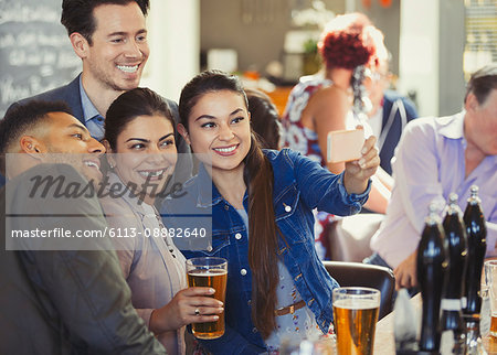 Playful friends drinking beer and taking selfie with camera phone at bar
