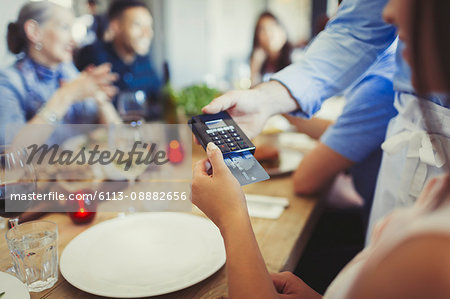 Woman with credit card paying waiter, using credit card reader at restaurant table