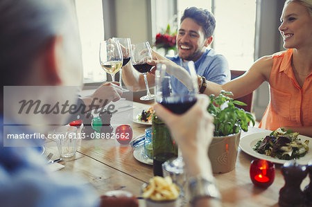 Smiling friends celebrating, toasting wine glasses at restaurant table