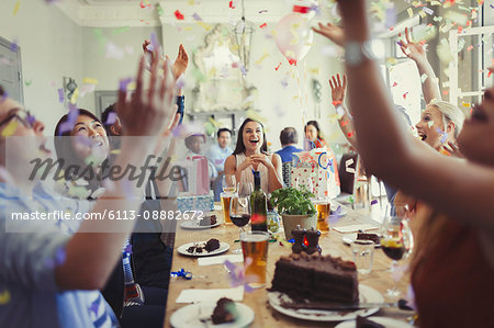 Friends celebrating birthday throwing confetti overhead at restaurant table