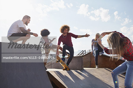 Woman photographing male friends skateboarding on ramp at sunny skate park