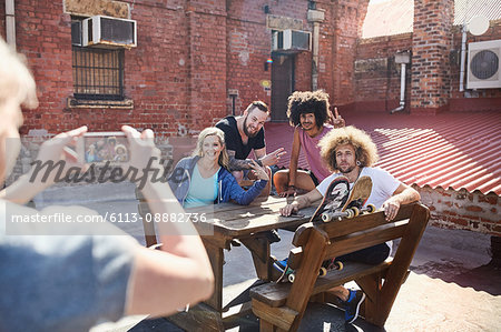 Woman with camera phone photographing friends hanging out on sunny urban rooftop