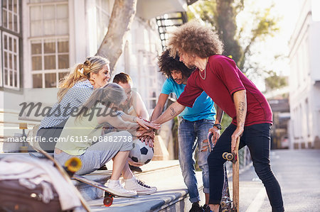 Friends with soccer ball and skateboards touching hands in huddle on urban steps