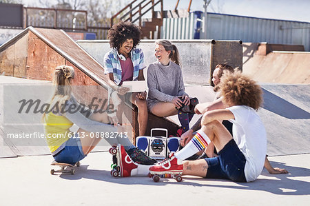 Friends in roller skates and on skateboard using digital tablet at sunny skate park
