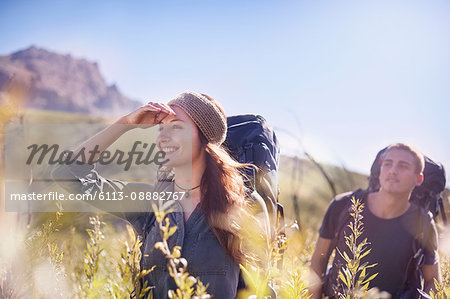 Smiling couple with backpacks hiking in sunny field