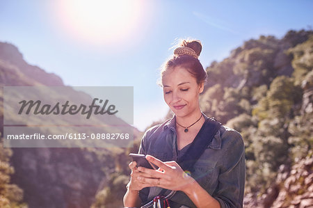 Young woman texting with cell phone below sunny cliffs