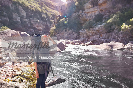 Young woman with backpack hiking at sunny remote stream
