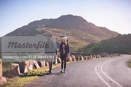 Young couple with backpacks hiking along remote, sunny road