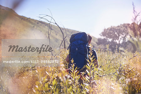 Young man with backpack hiking in sunny field