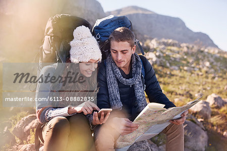 Young couple with backpacks hiking, resting and checking map and smart phone