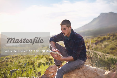 Young man using digital tablet on rock in sunny, remote valley