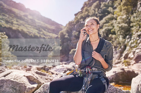 Young woman talking on cell phone below sunny, craggy cliffs